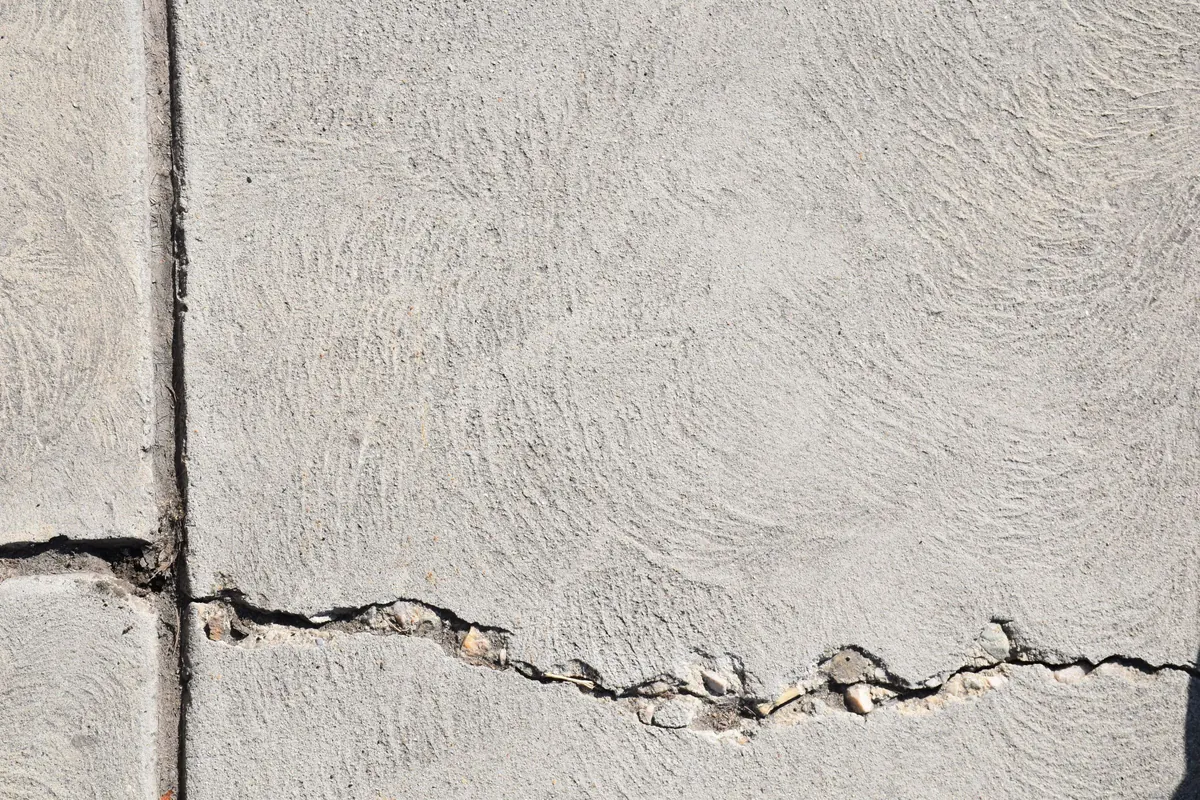 A jagged crack running across a pale concrete surface beside a straight joint line.