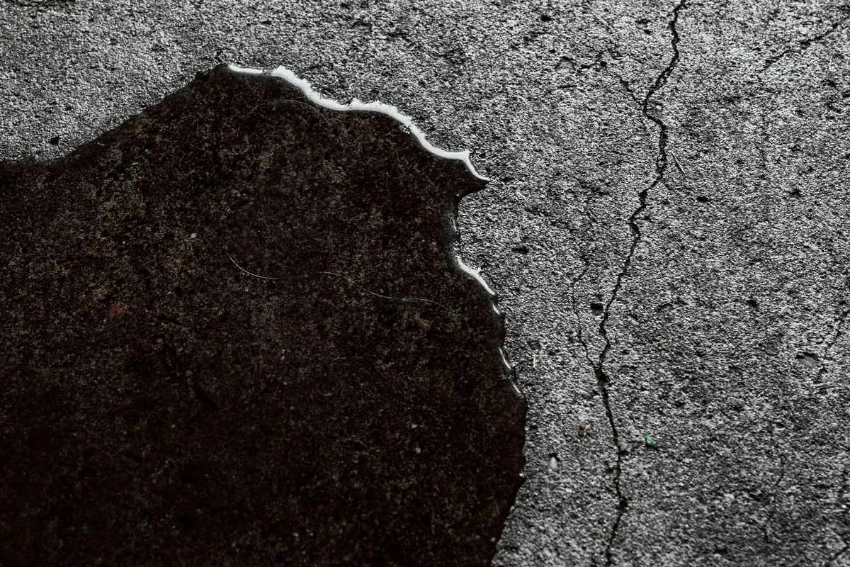 Water spreading across a gray concrete floor, with a thin crack running beside the wet patch.